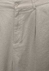 Pantalon en lin gris clair avec un pli devant, une fermeture à bouton unique et des détails de poches latérales. Texture lisse avec un aspect tissé.