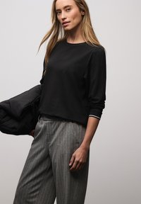 Czarna bluzka z długim rękawem i okrągłym dekoltem, z kontrastującymi białymi mankietami w paski. Połączona z szarymi spodniami w paski.