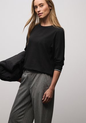 Czarna bluzka z długim rękawem i okrągłym dekoltem, z kontrastującymi białymi mankietami w paski. Połączona z szarymi spodniami w paski.