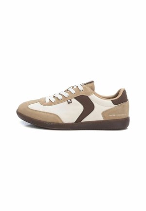 Zapato deportivo beige y blanco con materiales de ante y cuero, diseño curvado, acentos marrones, puntera redonda y suela de goma texturizada.