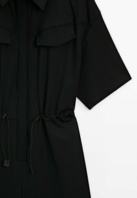 Zwarte short-sleeve jumpsuit met twee borstzakken, een cinched taille met trekkoorden en een soepele, lichtgewicht stof.