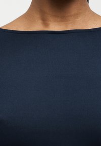 Κοντινό πλάνο ενός ατόμου που φοράει μπλε τοπ με λαιμόκοψη τύπου βάρκα, δείχνοντας το ντεκολτέ και το ανώτερο μέρος του στήθους.