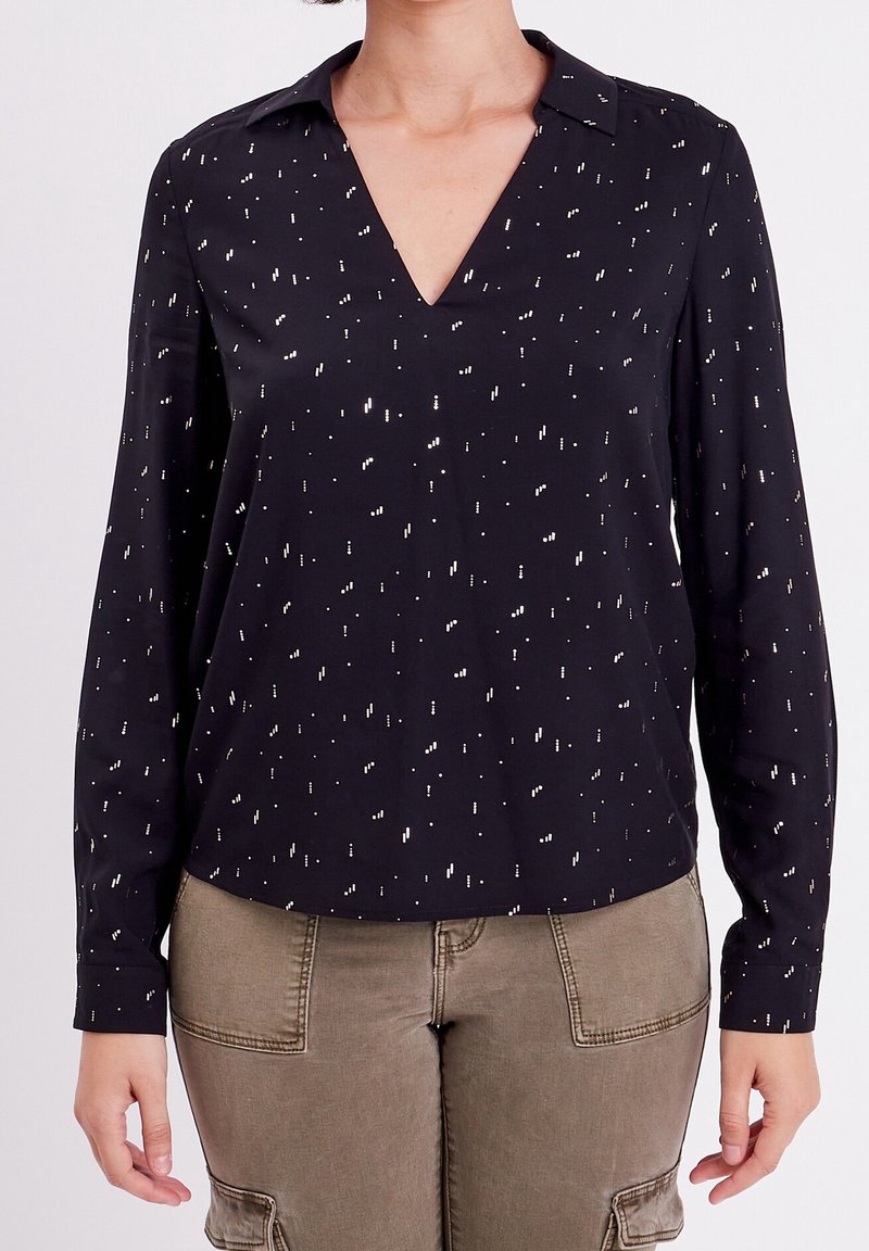 Blouse noire à manches longues avec un col en V, présentant des paillettes métalliques disposées de manière aléatoire. Confectionnée en tissu léger, avec une texture douce.