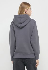 Felpa grigia di grandi dimensioni con cappuccio regolabile, polsini e orlo a costine. Il tessuto sembra morbido con una leggera texture spazzolata.