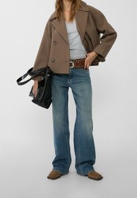 Brown double-breasted jacket, gray v-neck shirt, blue flared jeans with a brown studded belt, and black bag. Brown ankle boots.