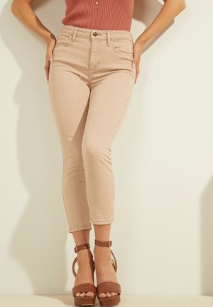 Vrouw draagt beige hooggetailleerde slim-fit jeans, bruine open-toe plateauhakken en een mouwloze geribbelde top in gedempte roodtint.