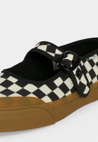 Μαύρο-άσπρο καρό παπούτσι Mary Jane με μαύρο λουράκι με αγκράφα και λαστιχένια σόλα, εμφανιζόμενο σε πλάγια όψη.