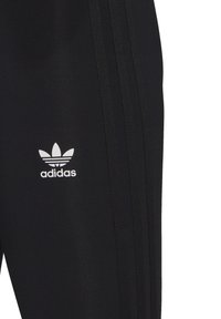 Melnas sporta bikses ar trim vertikālām svītrām, izgatavotas no gludas auduma, ar baltu Adidas logo augšējā kreisajā pusē.
