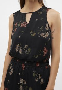 Černé bezramínkové šaty s výstřihem do V a malým detailem ve tvaru klíčové dírky. Obsahují květinový vzor v tlumených růžových a zelených tónech. Volný silueta, strukturovaná tkanina.