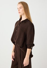 Brown button-up shirt with a textured finish, featuring a collar, gold button accents, and loose sleeves, paired with matching pants.