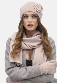 Căciulă tricotată roz cu accent floral, eșarfă asortată și mănuși; textură moale, design ajustat, ușoară, ideală pentru vreme mai rece.