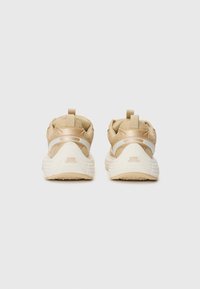 Un paio di sneaker sportive beige e bianche viste da dietro, con tessuto in rete, linguette di supporto e suole in gomma spesse con dettagli del logo.