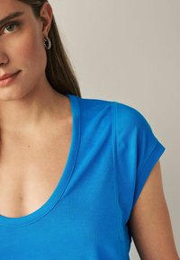 T-shirt blu brillante con maniche corte, scollatura profonda e superficie liscia. Presenta dettagli di cucitura sottili.