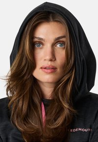 Felpa nera con cappuccio e finitura testurizzata, caratterizzata da un cordino rosa e un logo sul petto. Il modello mostra capelli naturali e un tono di pelle naturale.