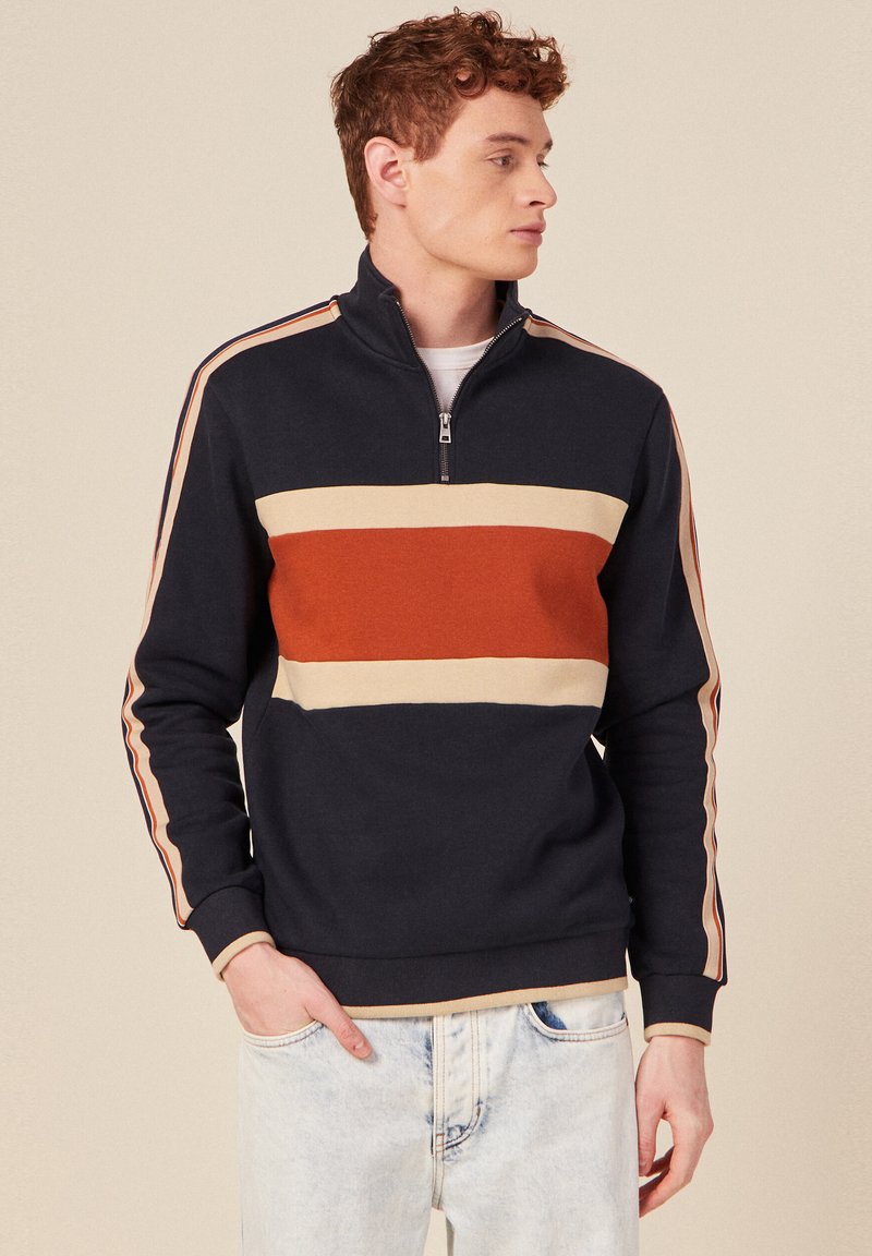 Felpa navy con collo a mezze zip, presenta strisce orizzontali in ruggine e crema, con strisce a contrasto sulle maniche. Tessuto morbido e texturizzato.