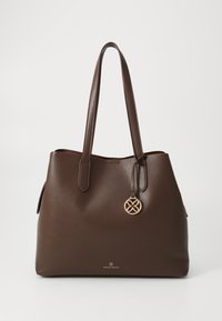 Sac fourre-tout en cuir marron avec deux poignées courtes, ornée d'un charme rond en or. Surface texturée et logo en relief en bas.