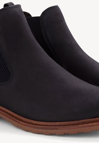 Botine negre din suede cu panouri elastice laterale și o talpă din cauciuc maro, având o textură netedă și un design cu vârf rotund.
