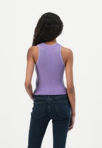 Lilla rebbede ermeløs topp med høy hals; tettsittende design med vertikale striper. Bært med mørke jeans, som viser en jevn tekstur.