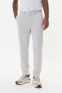 Pantalons tissés gris clair avec une coupe slim, dotés de poches latérales et d'une texture lisse, associés à des baskets de sport beiges.