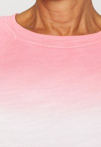 Collo e parte superiore del torace di una persona che indossa un maglione lavorato a maglia con sfumatura dal rosa al bianco, con cuciture visibili attorno al colletto.