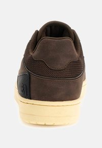 Sneaker marrone con una parte superiore texturizzata e dettagli in rete. Presenta una suola in gomma crema e un logo distintivo sul tallone.