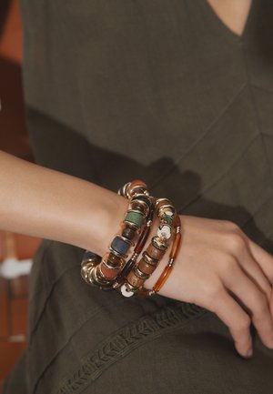Wrist adorned with multiple beaded bracelets featuring wood, metal, and patterned beads over a dark green outfit.