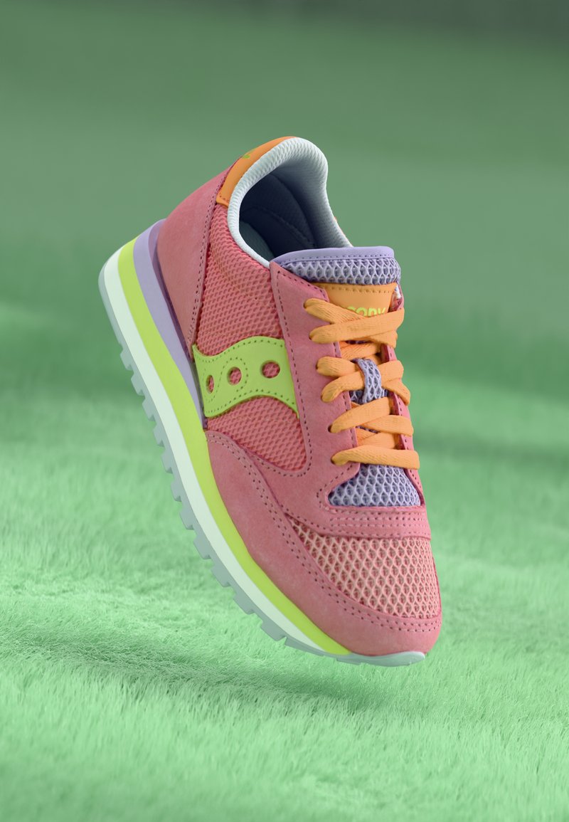 Lyserøde og lavendel sneakers lavet af net- og ruskindsmaterialer, med et orange accent, grøn logo og en hvid sål med en neongrøn stripe.