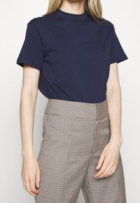 Marineblå bomulds t-shirt med korte ærmer og høj halsudskæring, parret med højtaljede ternede bukser i beige og brune nuancer.