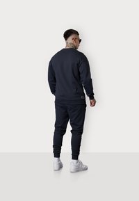 Navy Sweatshirt- und Jogginganzug-Set, aus weichem Stoff, mit gerippten Bündchen, Rundhalsausschnitt und weißen Sneakers. Rückansicht mit minimalistischem Design.