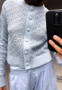 Svijetloplava pletena kardigan s teksturiranim dijamantnim uzorkom, rebrastim rubom i pet velikih, okruglih dugmadi sprijeda.