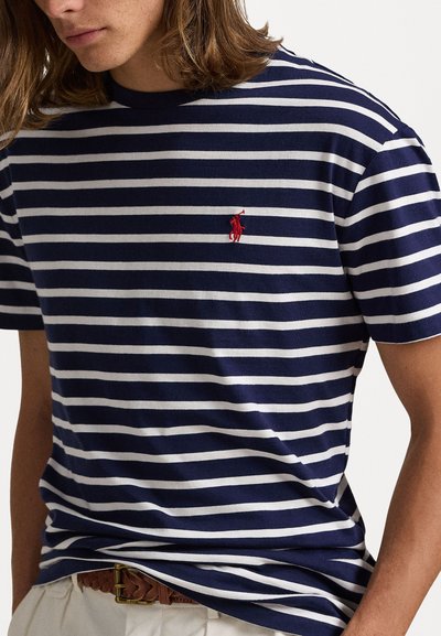 Námořnicky modré a bílé pruhované tričko s krátkým rukávem a kulatým výstřihem, s malým červeným vyšitým logem na levé hrudi.