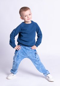 Niebieska bluza z długimi rękawami w połączeniu z jasnoniebieskimi, teksturowanymi spodniami typu cargo z bocznymi kieszeniami oraz białymi sportowymi butami.