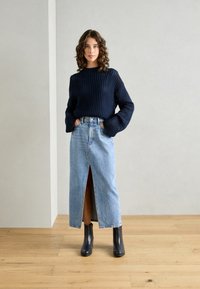 Pulover din lână bleumarin, cu mâneci largi, asortat cu o fustă din denim albastru deschis, cu o fanta frontală și botine negre.