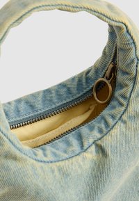 Lichtblauwe denim tas met een ronde handgreep en een gedeeltelijk open rits die een beige stoffen binnenzak laat zien.