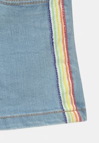 Pantalones cortos de tejido vaquero cortados en color azul, con un panel lateral que presenta rayas de arcoíris. La costura en marrón claro complementa el diseño.