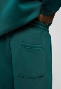 Teal sweatpants van zacht materiaal, met een elastische tailleband en een enkele achterzak met een gestikte randafwerking.