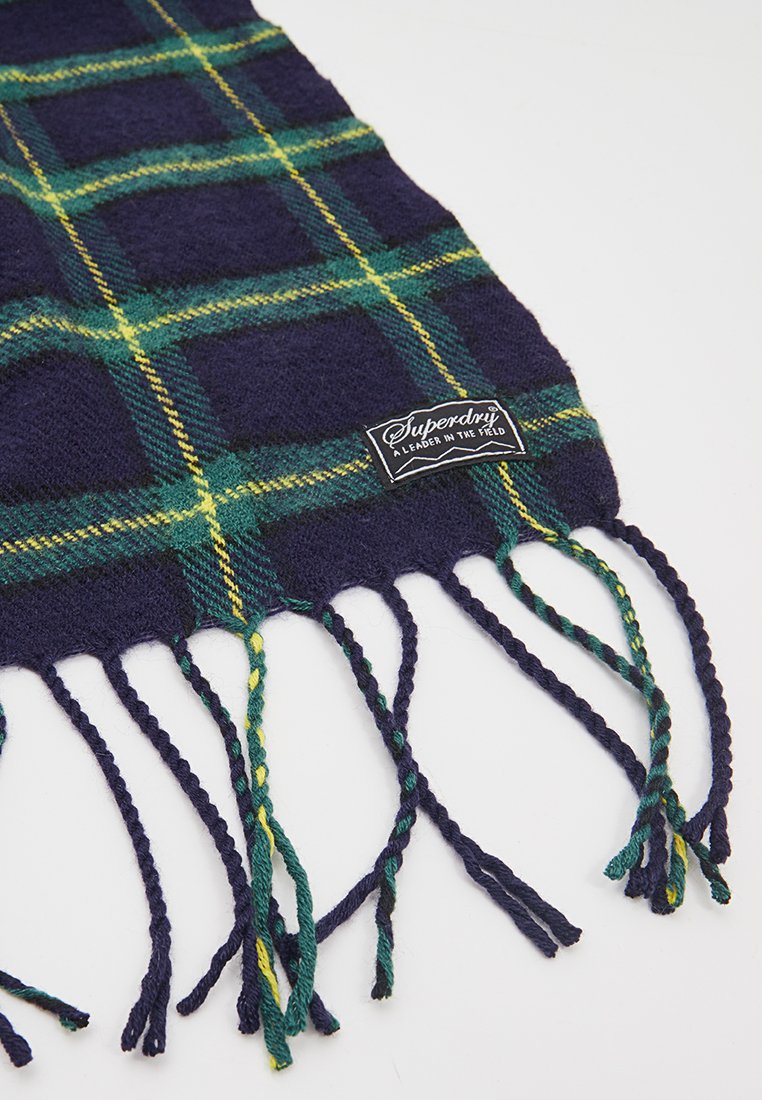 Écharpe en tartan bleu marine et vert en tissu doux. Présente des extrémités à franges avec des fils torsadés. Comprend une étiquette de marque avec du texte.