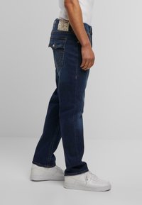 Donkerblauwe denim jeans met een recht model, voorzien van achterzakken met stikseldetails en een merklabel op de tailleband.