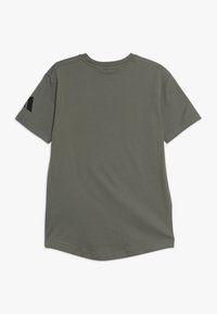 Harmaa lyhythihainen T-paita, jossa on pyöreä kaula-aukko ja sileä pinta; vasemmassa hihassa on musta logotunnus.