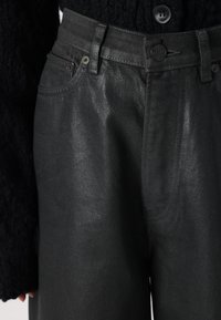 Pantalon en denim noir avec une finition texturée, doté d'une fermeture à bouton, d'un design à cinq poches et d'une taille haute.