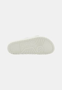 Suela de zapatilla deportiva blanca con patrones texturizados, surcos profundos para tracción y un diseño de logo prominente en el costado. Líneas horizontales y verticales visibles.