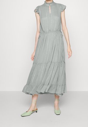 Vestido midi sin mangas de color gris claro con cuello y dobladillo volante, cintura fruncida, acompañado de zapatos de tacón bajo en verde pálido con cordones.
