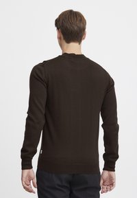 Maglione lavorato a maglia marrone con maniche lunghe, scollo rotondo e polsini a coste. Tessuto uniforme con un piccolo etichetta logo sull'orlo dietro.