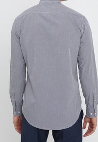 Košile s dlouhými rukávy v námořnické modré a bílé kostkované vzoru. Má zaoblený lem a manžety na knoflíky s kontrastními knoflíky.