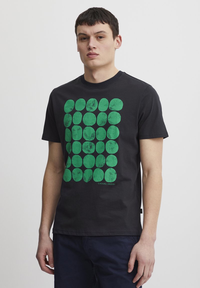 Sort bomulds t-shirt med et gitter af teksturerede grønne ovale former på fronten, med rund halsudskæring og korte ærmer.