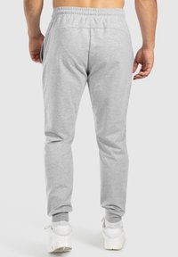 Pantalon de survêtement gris avec une taille élastique, coupe ajustée et poches latérales, associé à des baskets blanches. Tissu doux avec une texture lisse.