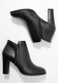 Botas de tobillo negras con una textura sintética suave, cremalleras laterales y un tacón bloque a rayas. Silueta Curvada y detalles de costura mínimos.