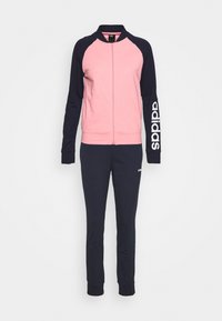 Różowo-czarny dres Adidas z kurtką na zamek błyskawiczny, czarne rękawy z logo Adidas na prawej ręce oraz czarne spodnie z małym logo na udzie.