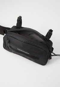 Black nylon shoulder bag featuring multiple zippered compartments, adjustable straps, and sleek, textured surface. Minimalist design with logo.