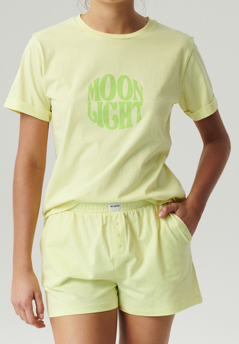 Jasnożółta bawełniana koszulka z grafiką "MOON LIGHT" w zielonym kolorze. Pasujące szorty z elastycznym wstążką w talii i dwiema przednimi kieszeniami, również jasnożółte.